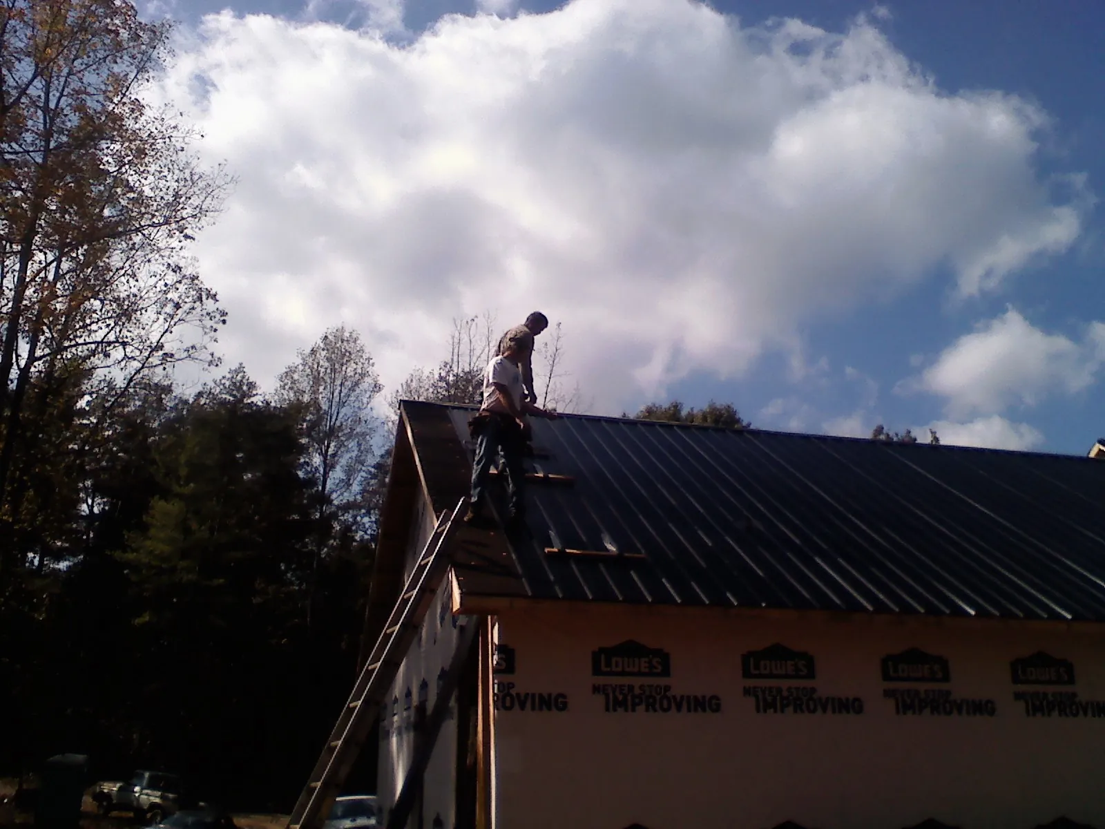Roofer fastening dark metal panels high against a cloudy sky, from a Roof Inspection job in Cumberland